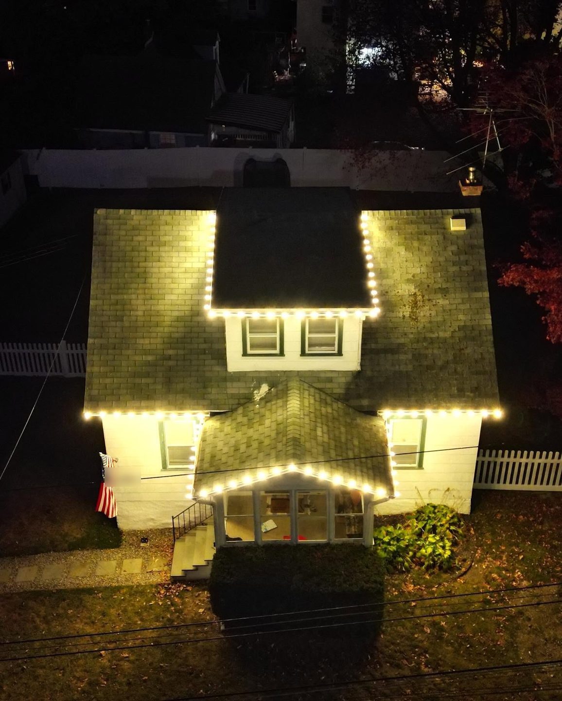 Warm white lights on the roofline, dormer, and front porch, seen from above