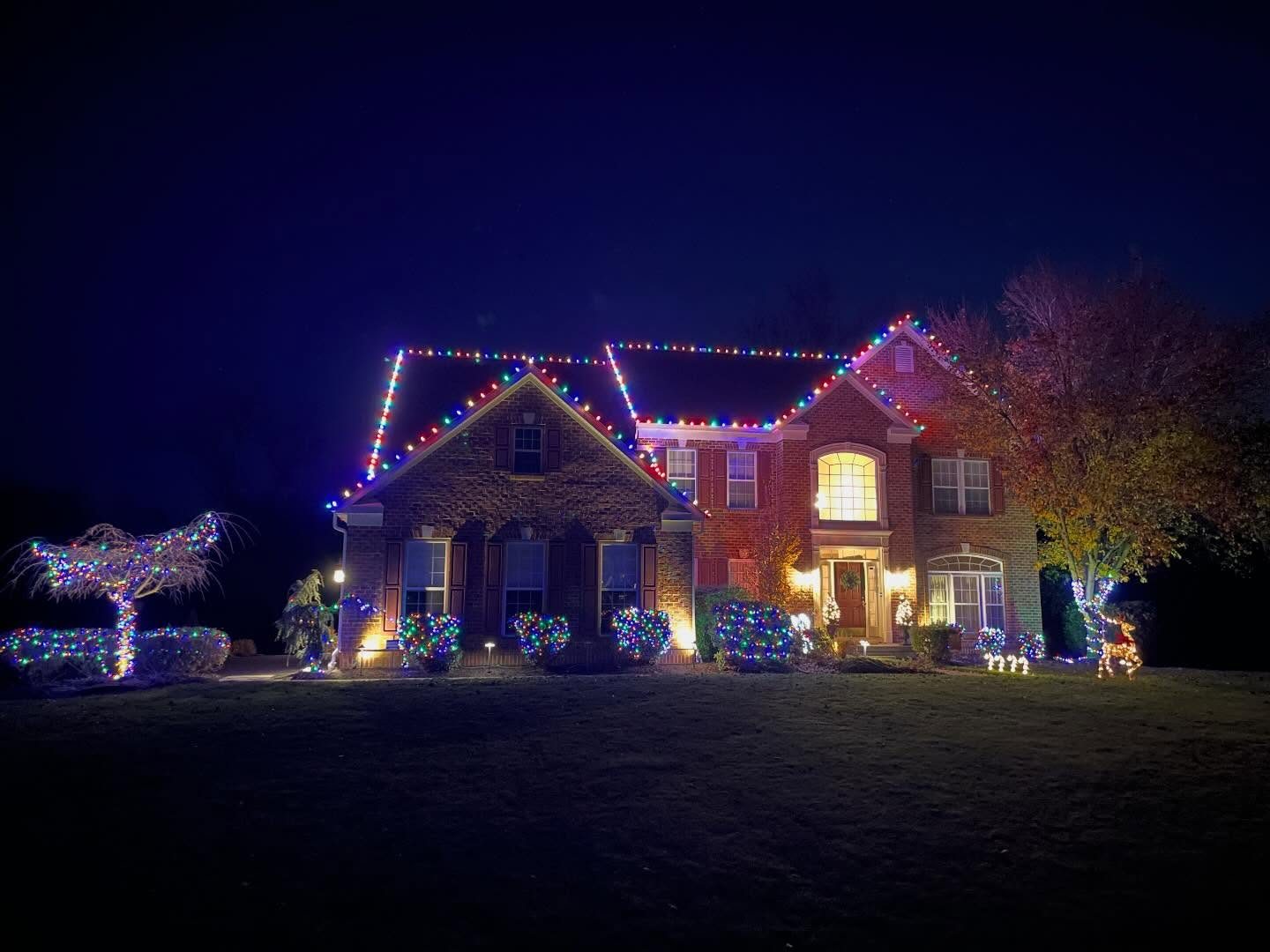 Multicolor roofline lights with wrapped shrubs and trees on a brick colonial