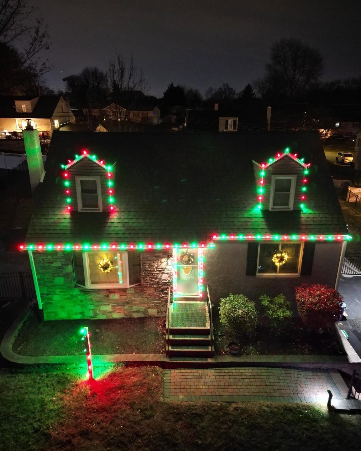 Red and green C9 lights outlining dormers, roofline, and front door, seen from above