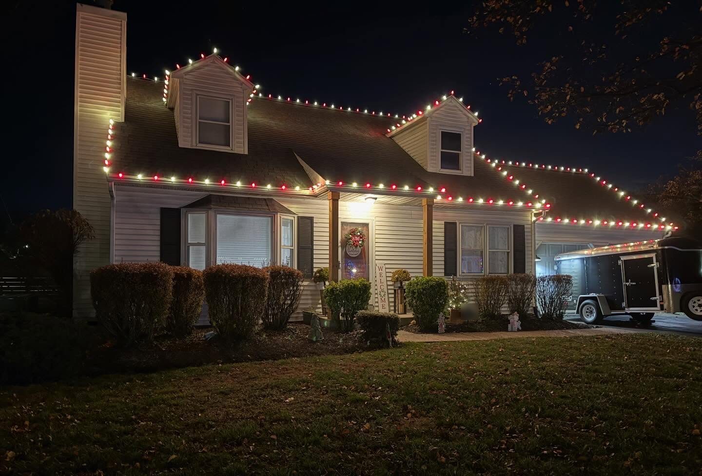 Red and warm white C9 lights on the roofline and dormers of a Cape Cod