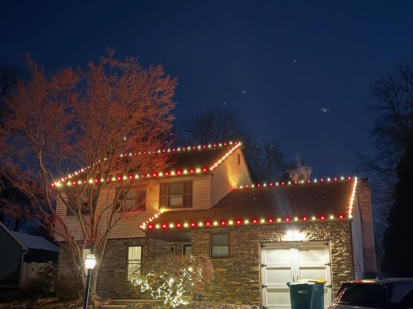Red and warm white roofline lights on a two story stone and siding home
